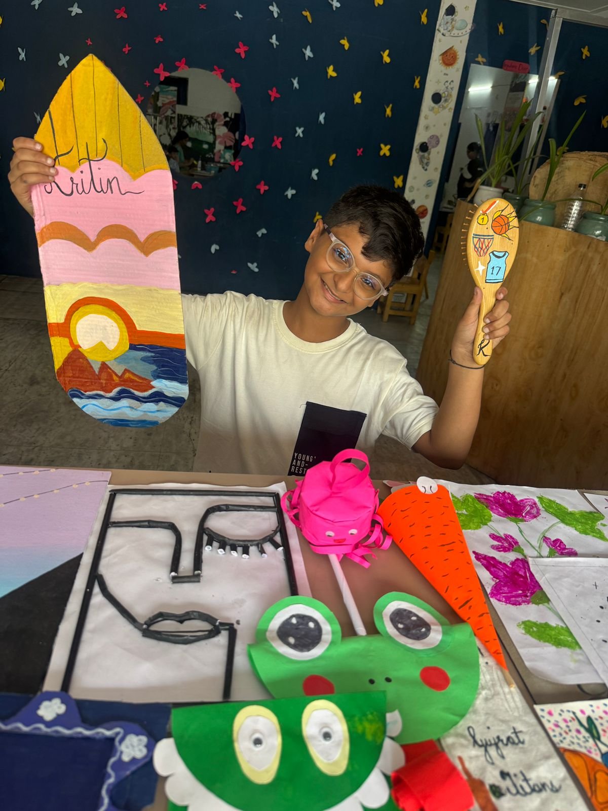 A boy holding his hand-painted sunset artwork and a decorated wooden spoon