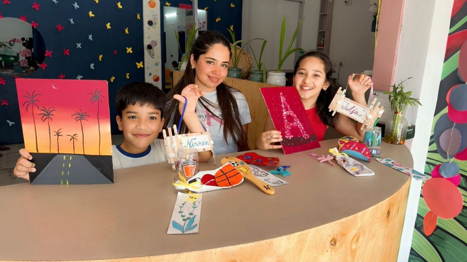 A caregiver with two children showing their finished paintings and keepsakes